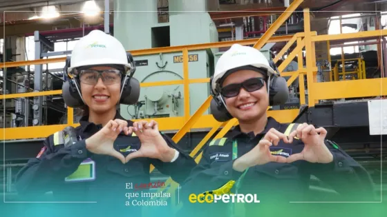 Dos trabajadoras de Ecopetrol con casco, gafas y uniforme de seguridad forman un corazón con sus manos en una planta industrial. La imagen representa el compromiso y la energía del talento humano que impulsa a Colombia, bajo el lema ‘El corazón que impulsa a Colombia’