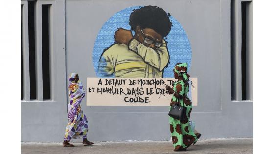 Un grupo de personas camina junto a un set de graffitis que representan los pasos higiénicos, que se deben seguir para luchar contra COVID-19 en Dakar, Senegal.