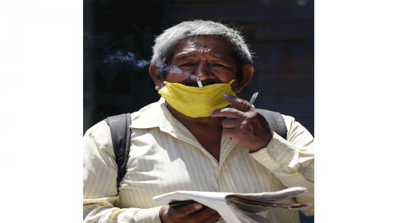 Un hombre fuma a través de una mascarilla hecha con un paño de cocina, el 14 de abril de 2020, en Lima (Perú). Ante la necesidad de usar tapabocas o mascarillas para evitar el contagio de coronavirus, y la escasez debido a la alta demanda, los ciudadanos han recurrido a la creatividad para suplir estos elementos básicos. EFE/Paolo Aguilar